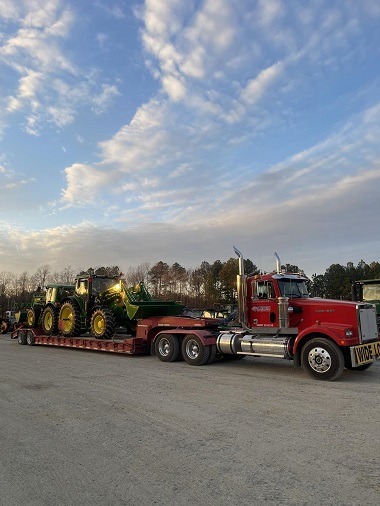 Red semi-truck hauling three farm tractors